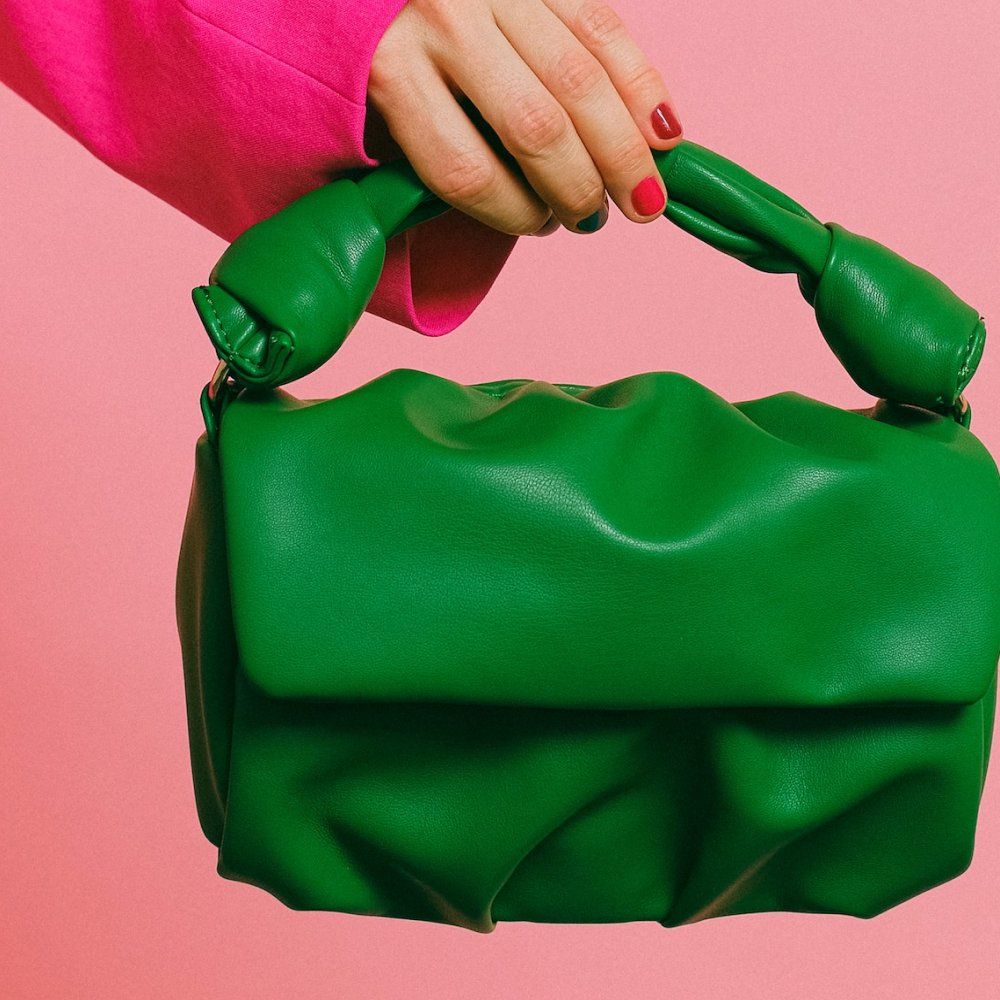 Hand holding a bright green handbag against a pink background