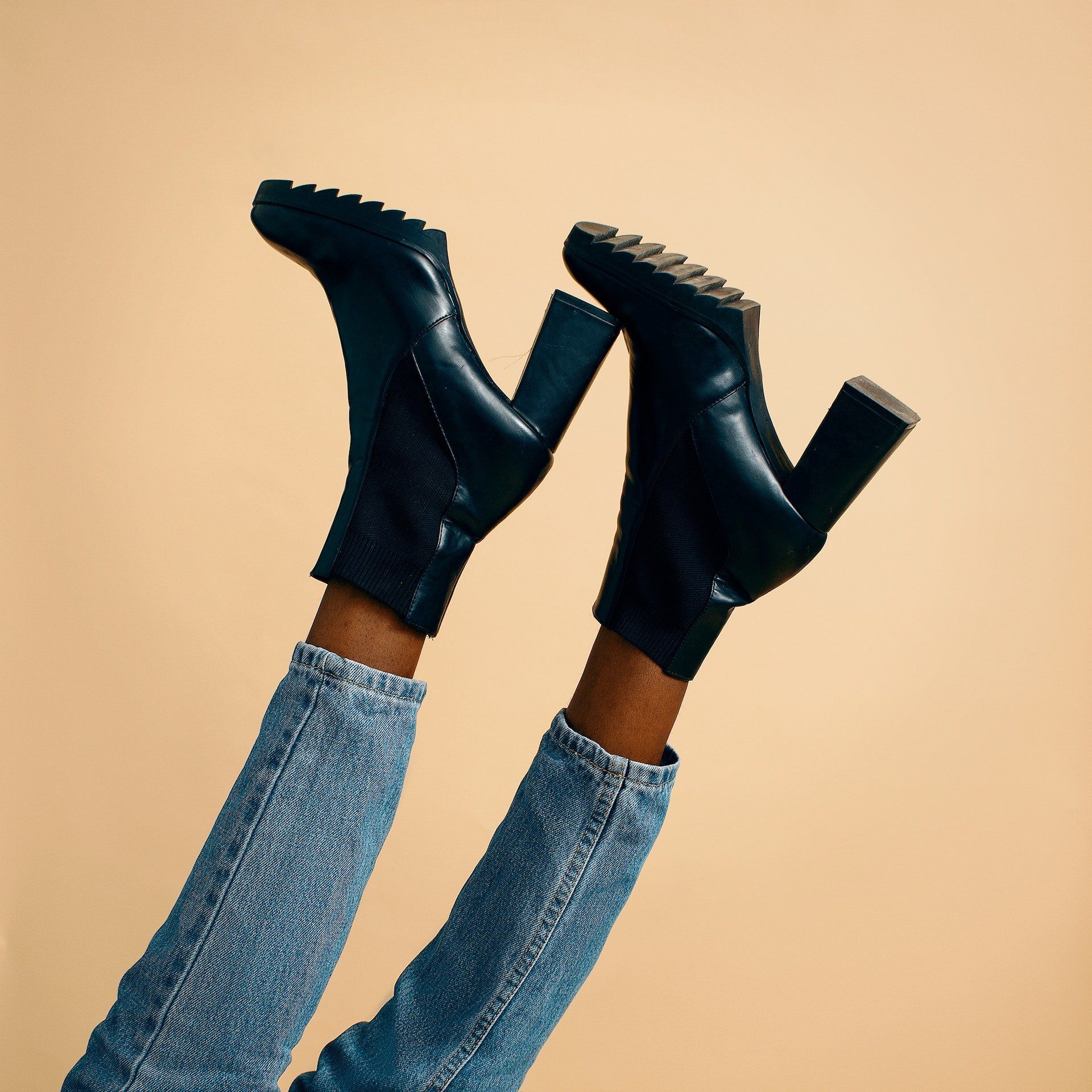 Black ankle boots and blue jeans legs raised against a beige background