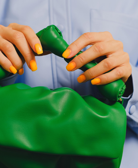 Hands with yellow nails holding a green bag close-up