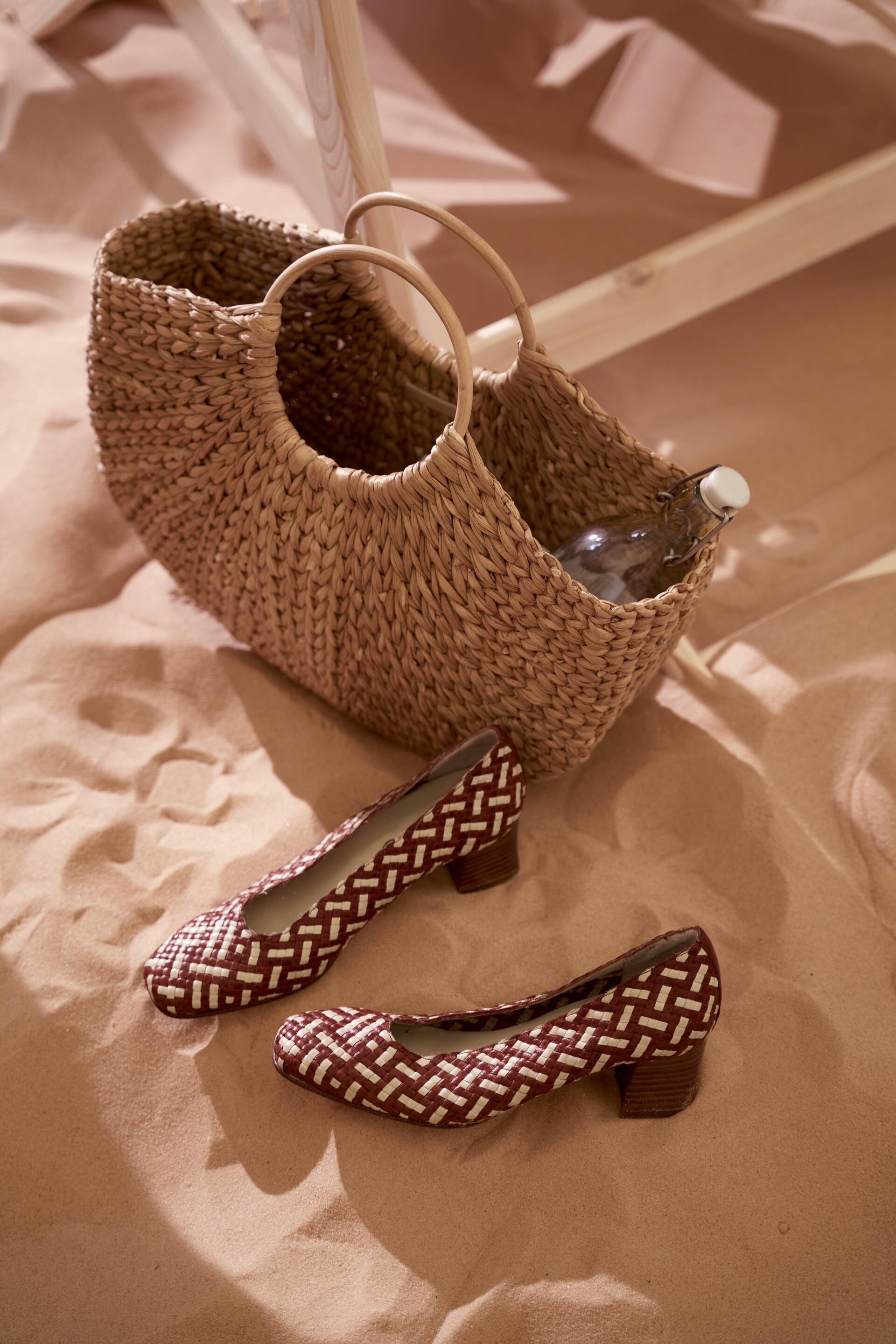 Two woven wedge sandals with patterned bows displayed on a beige fabric surface.