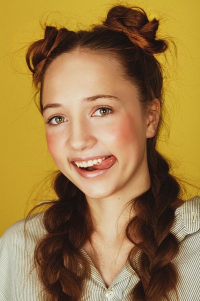 Smiling person with braided hair against a bright yellow background