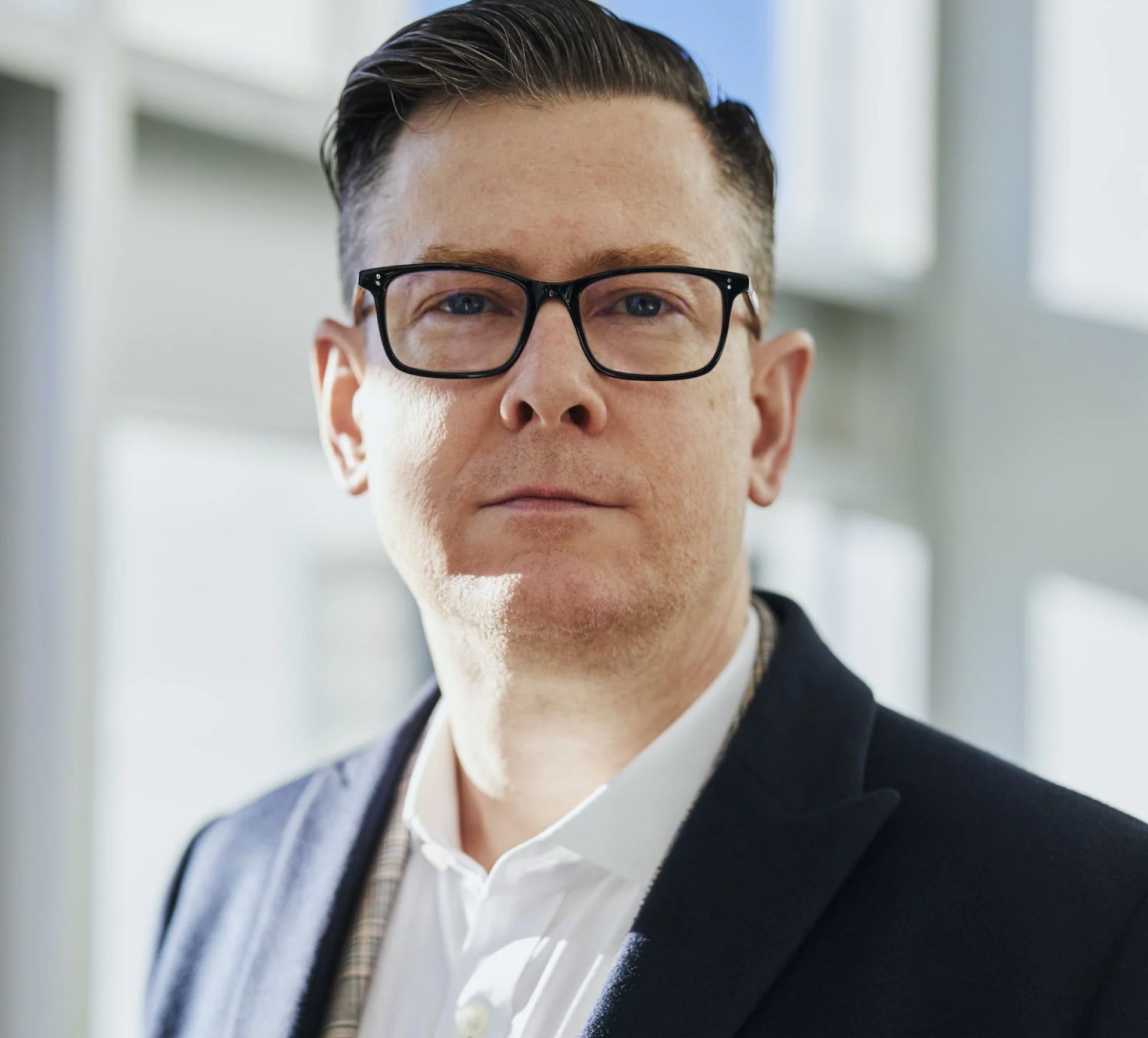 Man in glasses and suit jacket, looking at the camera. Soft lighting, neutral background.