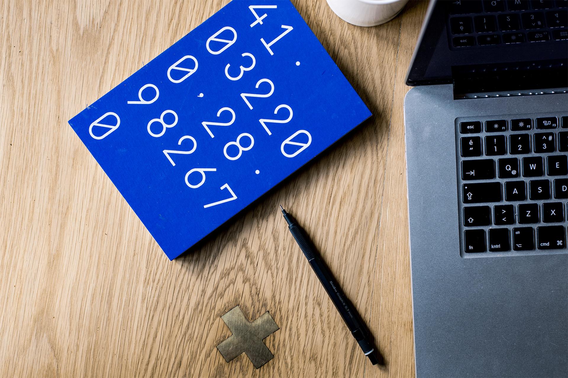 a blue book with numbers on it next to a pen and a laptop