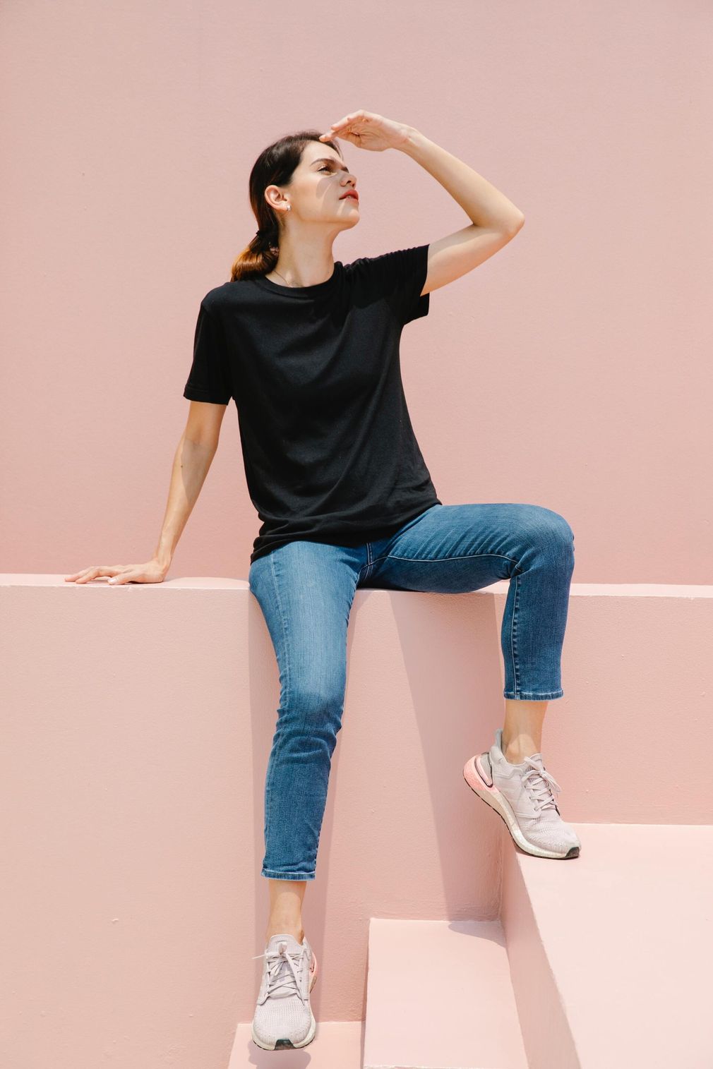 Woman in black shirt and jeans posing on pink steps against a pastel pink wall