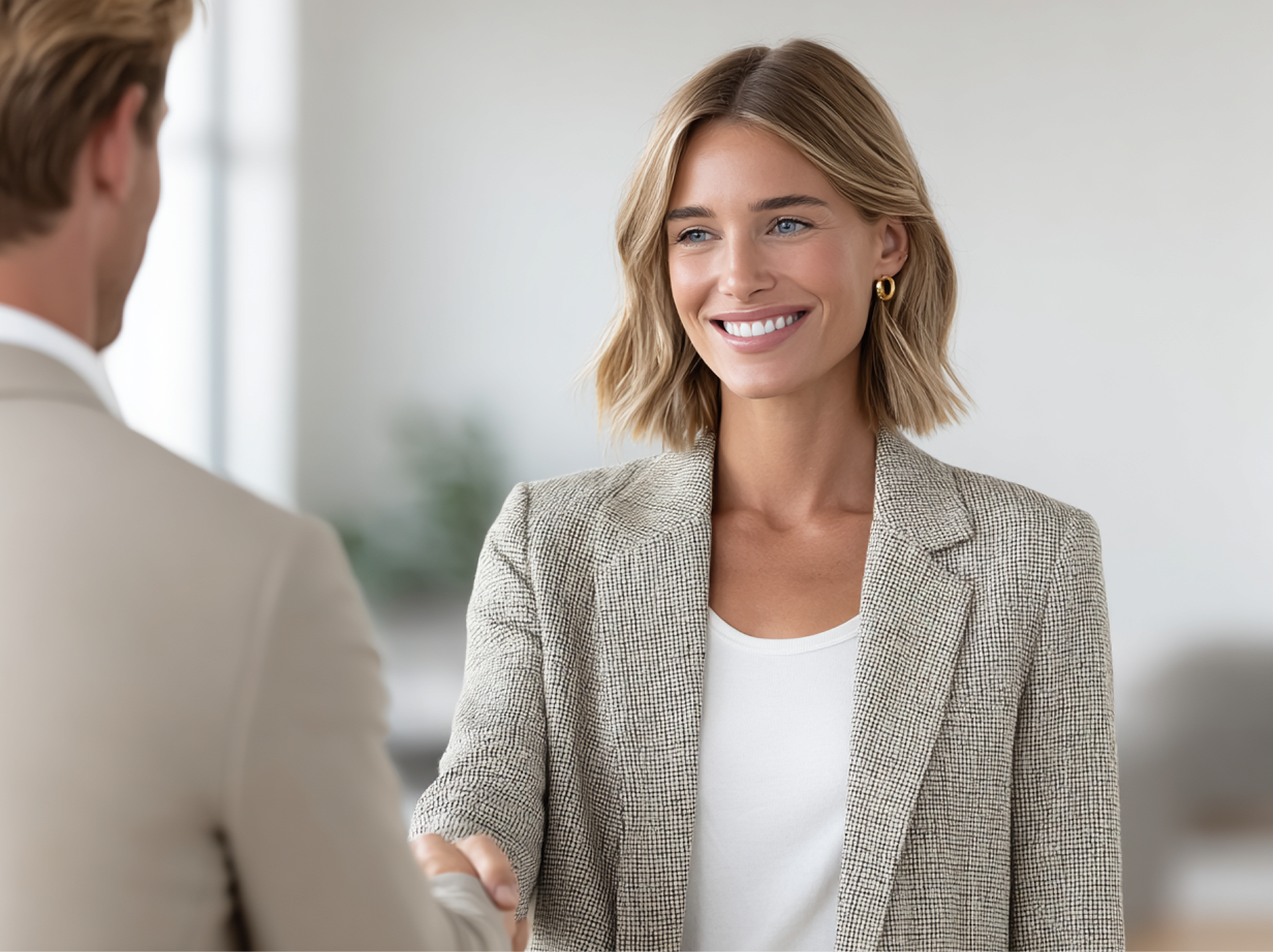 Una donna in blazer stringe la mano a una persona, sorridendo in una stanza luminosa.