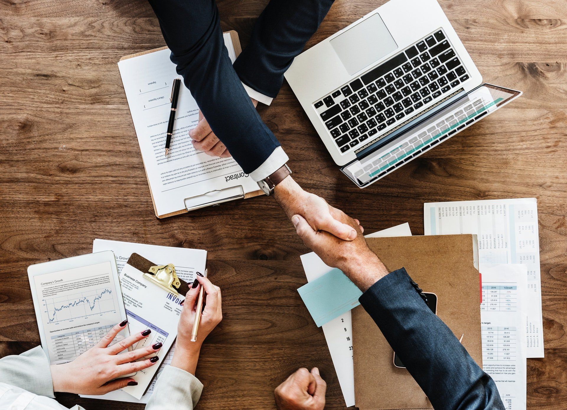 A man and a woman are shaking hands over a wooden table.