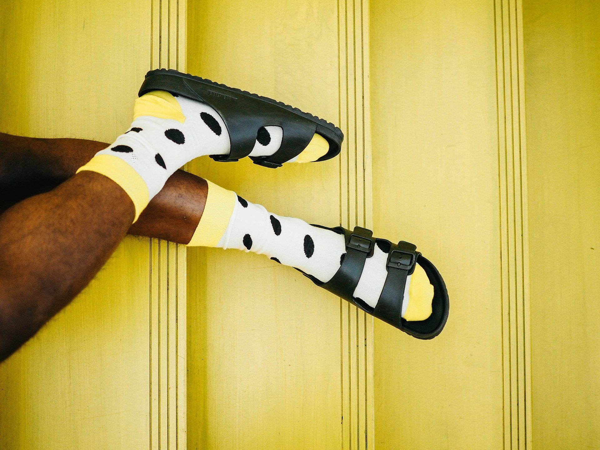 A person wearing yellow and white socks and black sandals.