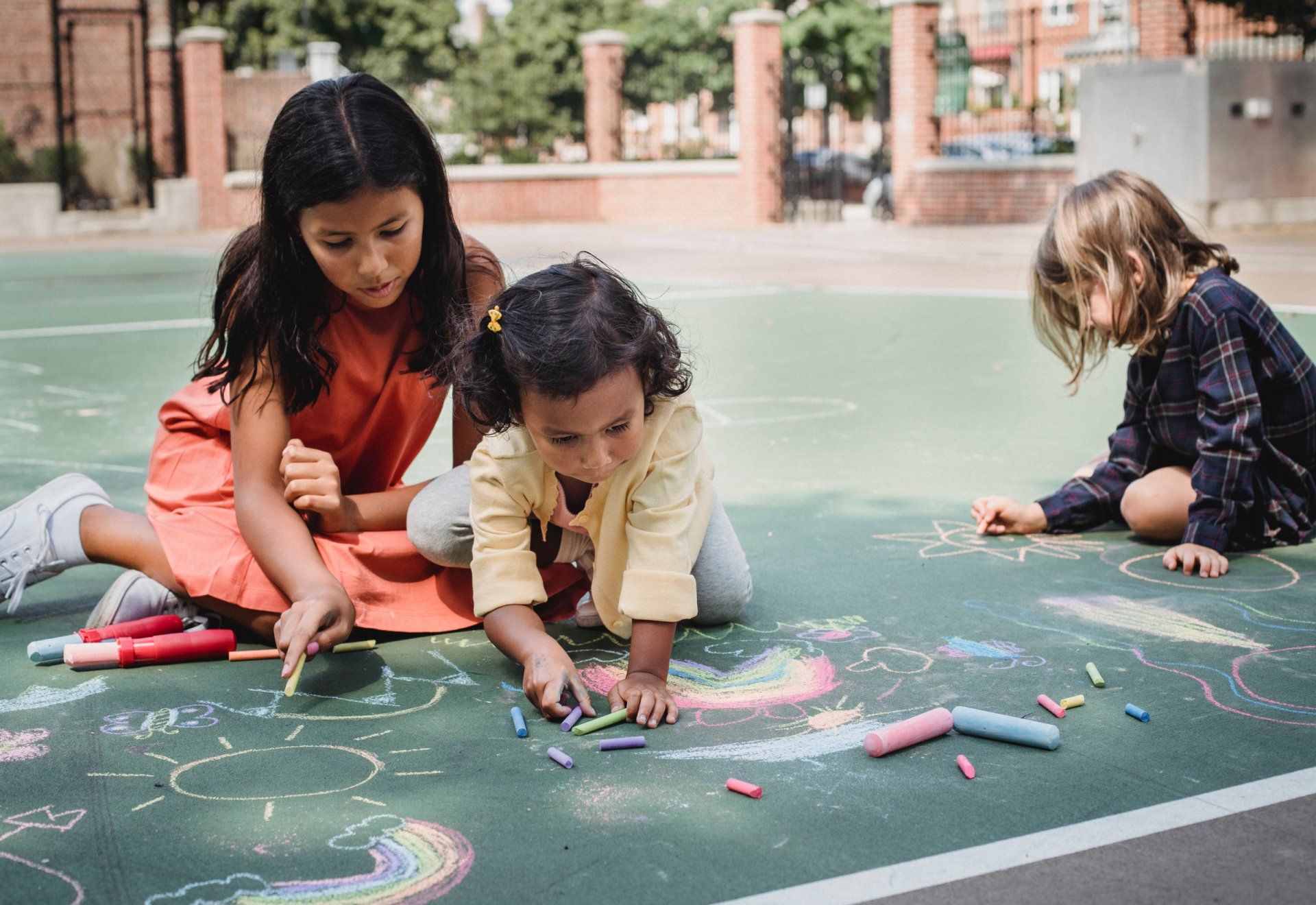 A group of children are sitting on the ground drawing with chalk.