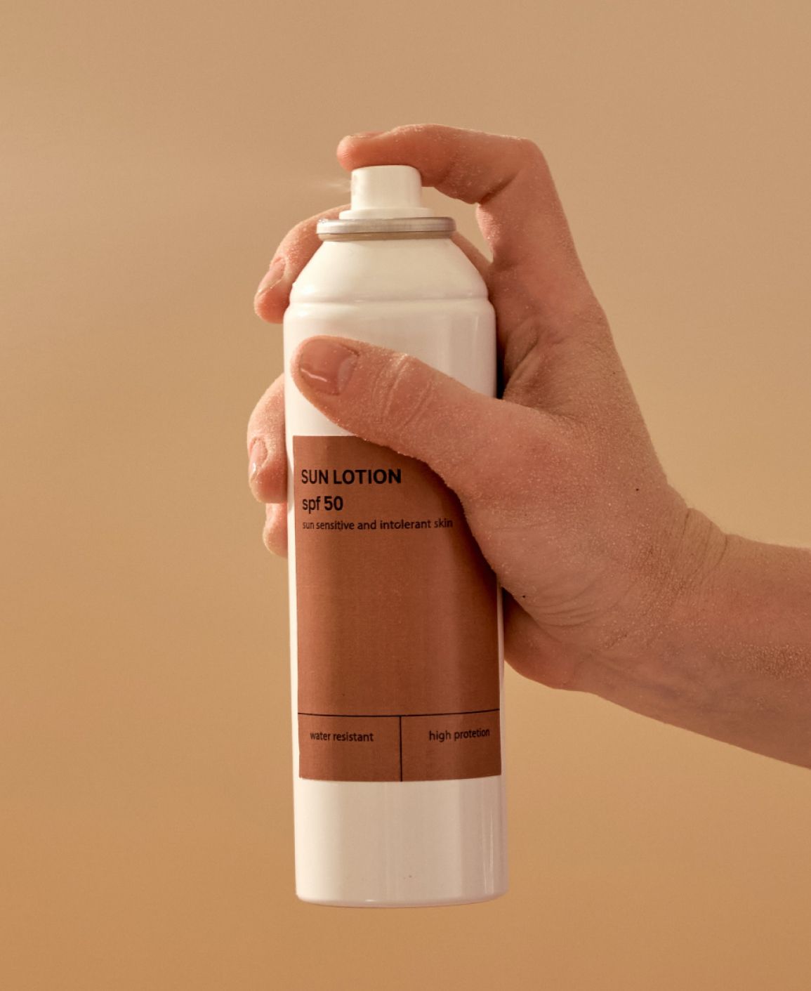 Hand spraying sunscreen lotion from a white can with a brown label.