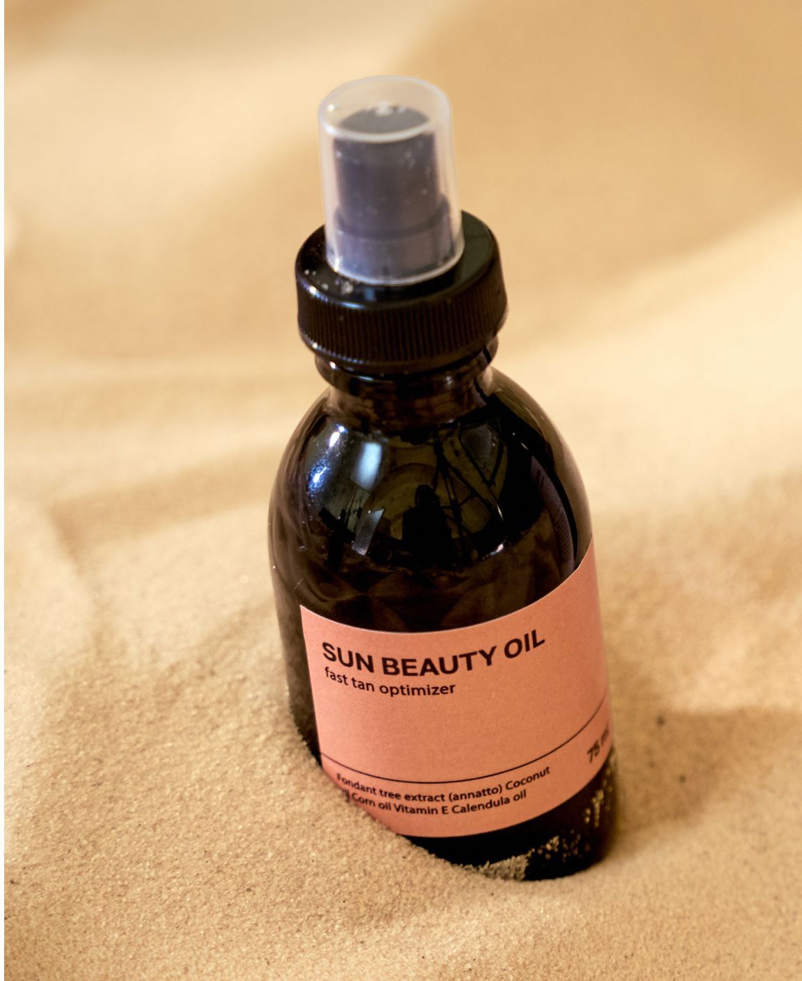 Dark bottle of Sun Beauty Oil with spray nozzle, on sand.