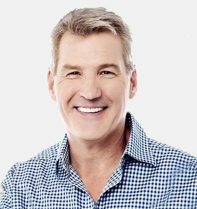 Man with short gray hair, smiling, wearing a blue and white checkered shirt against a white background.