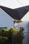 Blue-sided house with dark roof, rose bushes in front, and a chain-link fence.