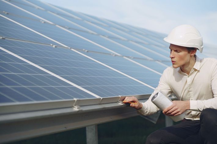 Technician inspecting rooftop solar panels beside a white hard hat