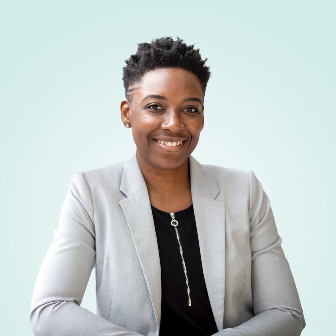 Person with short dark hair smiling, wearing a gray blazer over a black top.