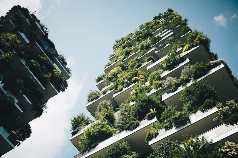 Two high-rise apartment buildings covered in lush greenery, under a bright blue sky.