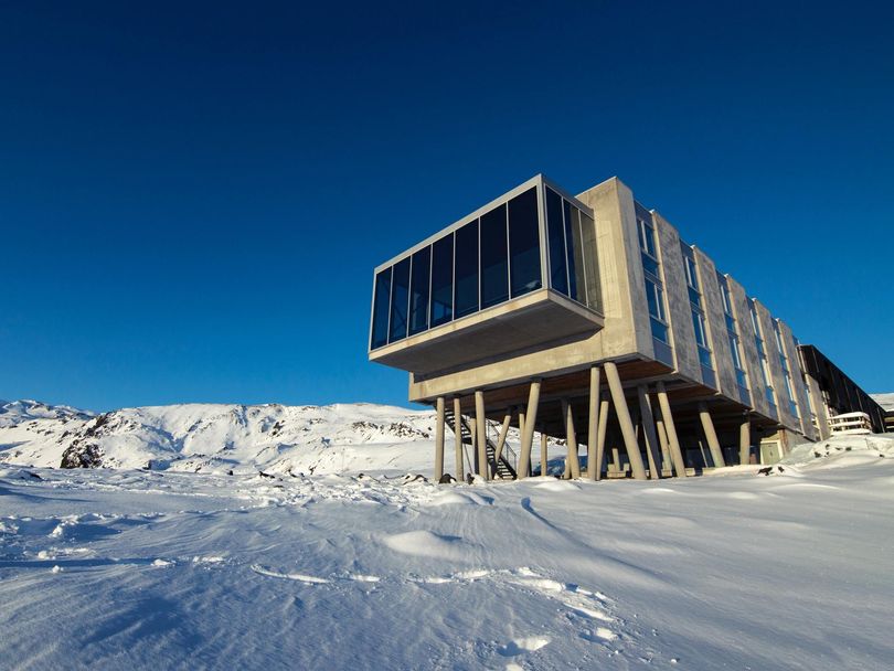 Modern hotel building on stilts in a snowy landscape under a bright blue sky.