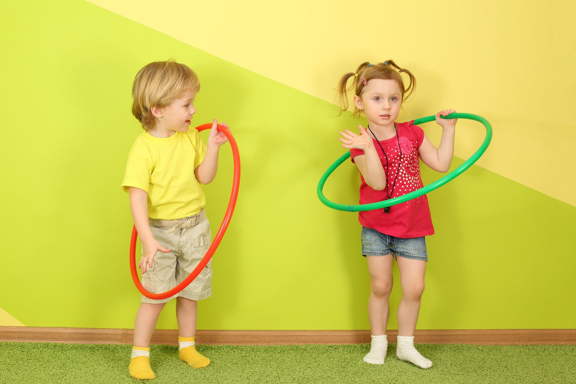 A boy and a girl are playing with hula hoops in a room.