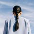 Woman in light blue blazer, black braided ponytail against a blue sky.