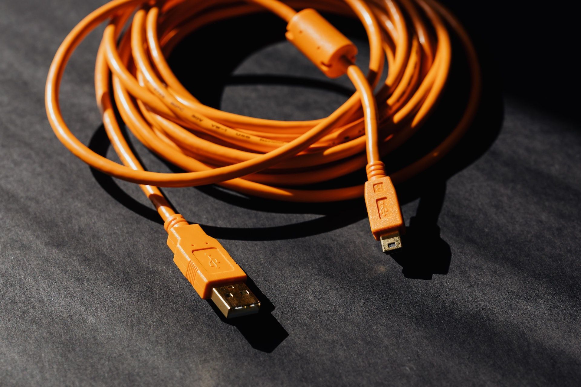 Coiled orange USB cable with two connectors on a dark fabric surface