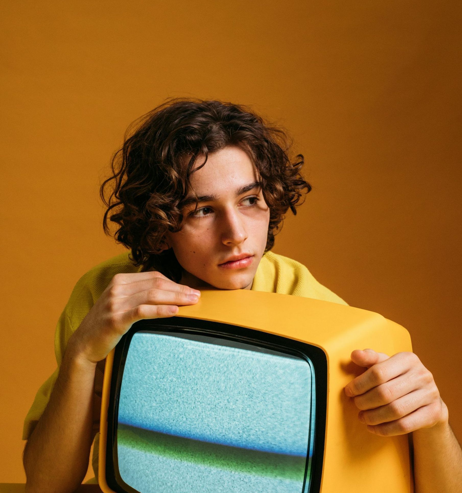 A young man is holding a yellow television in his hands.