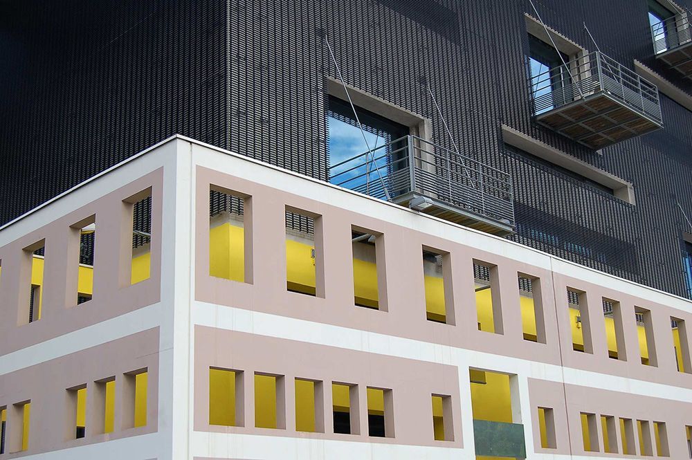 Modern white building with rows of yellow windows beside a dark, patterned high-rise.