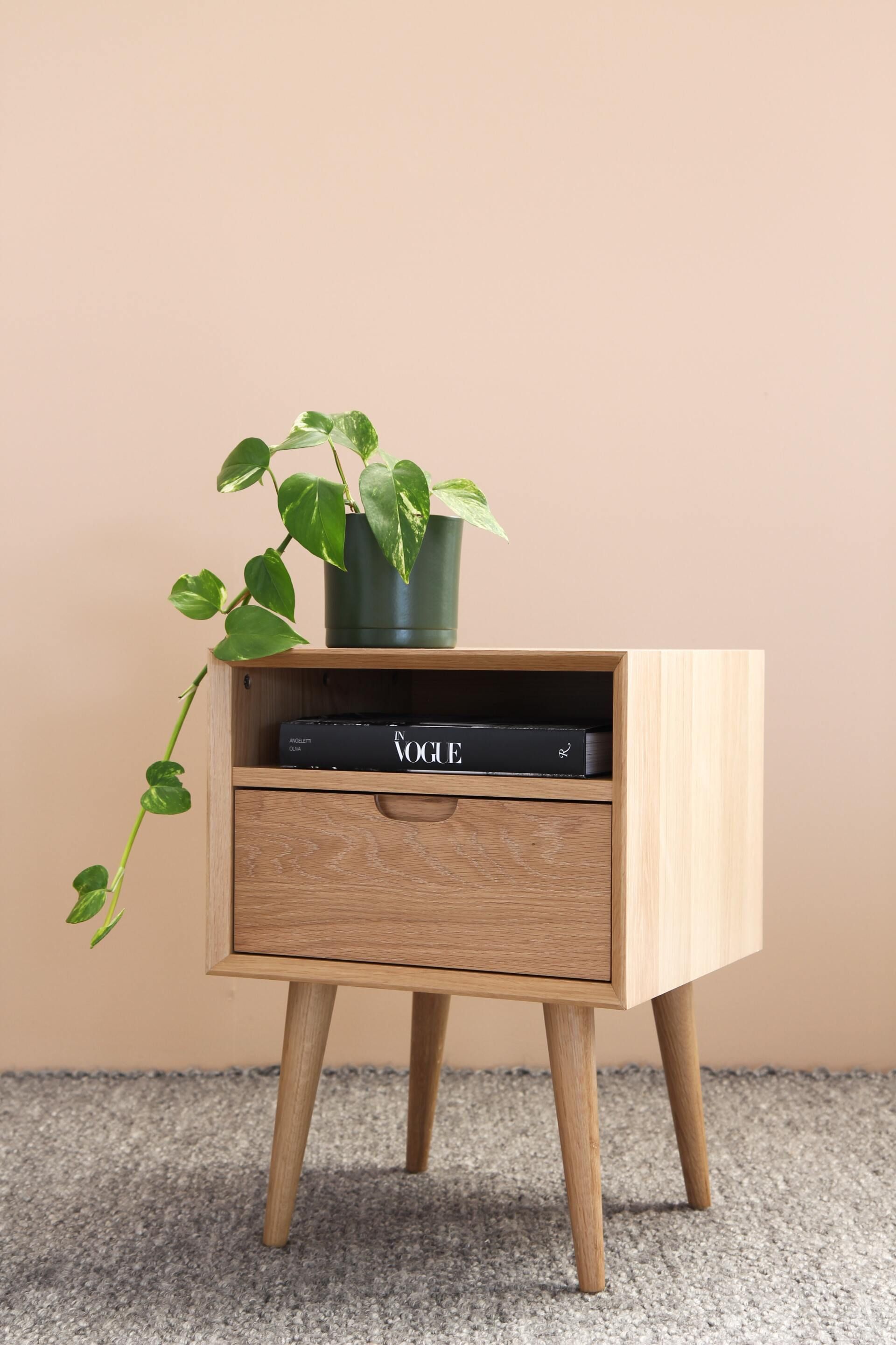 Wooden nightstand with plant, drawer, and AV equipment on a light beige background.