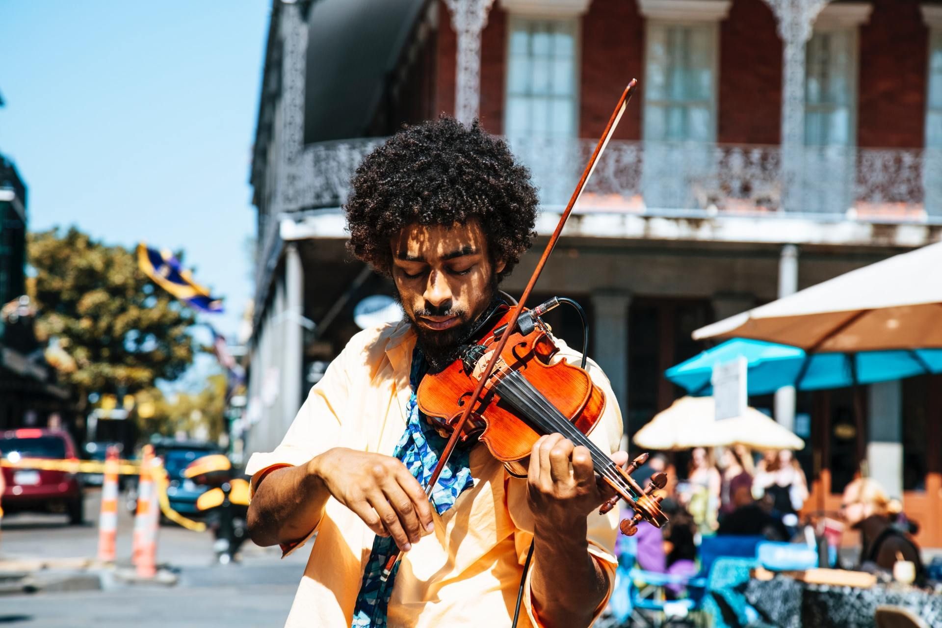 Street violinist playing outdoors in bright sunlight, with a building and umbrellas in the background