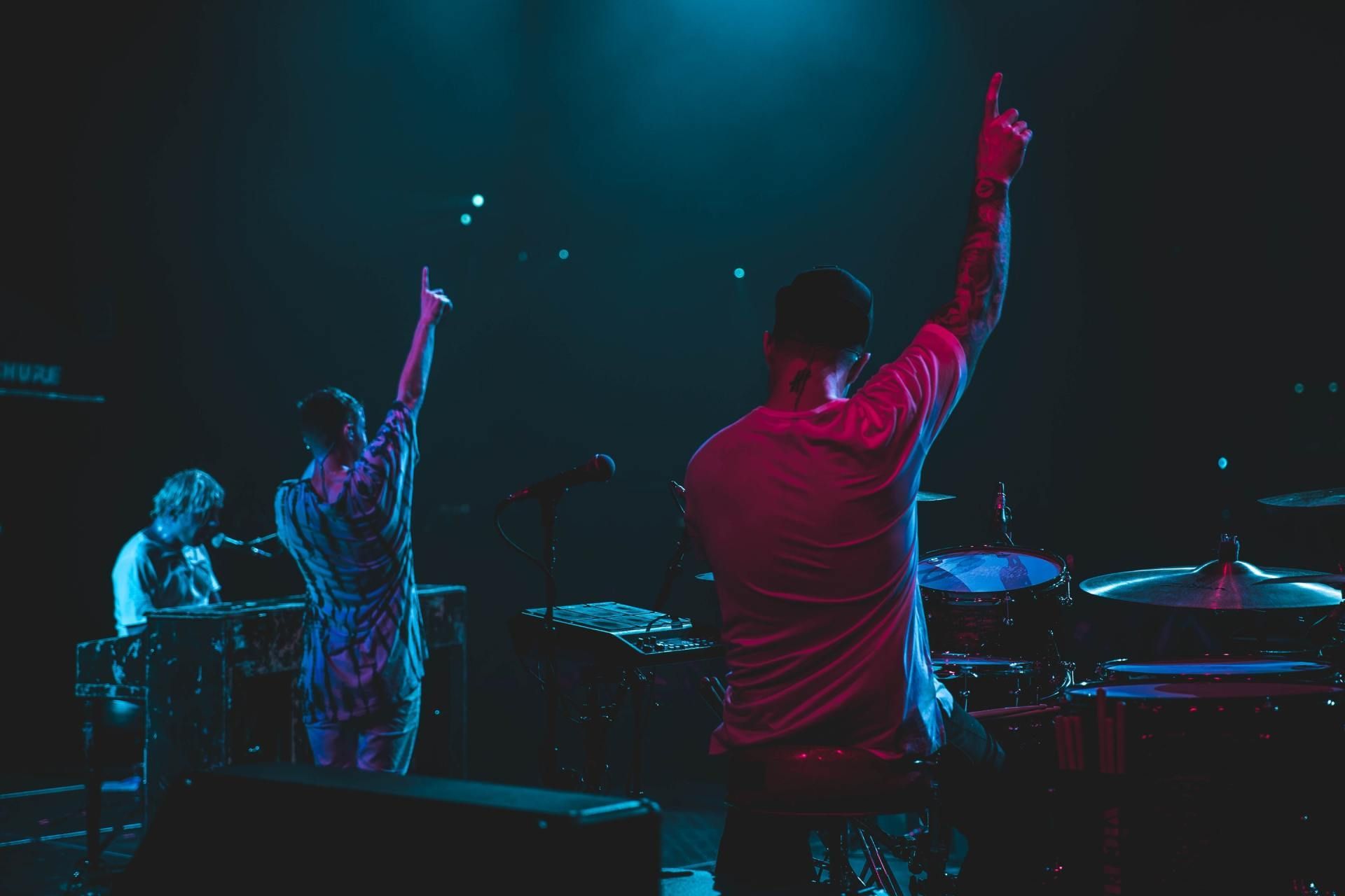 Musicians on stage with raised arms under blue and pink concert lights