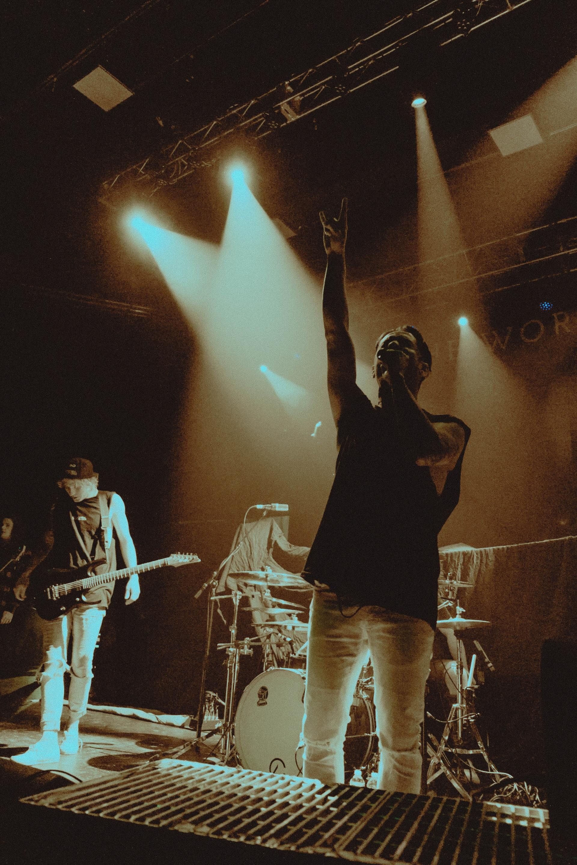 Band performing on stage under warm spotlights, singer raising an arm at center front