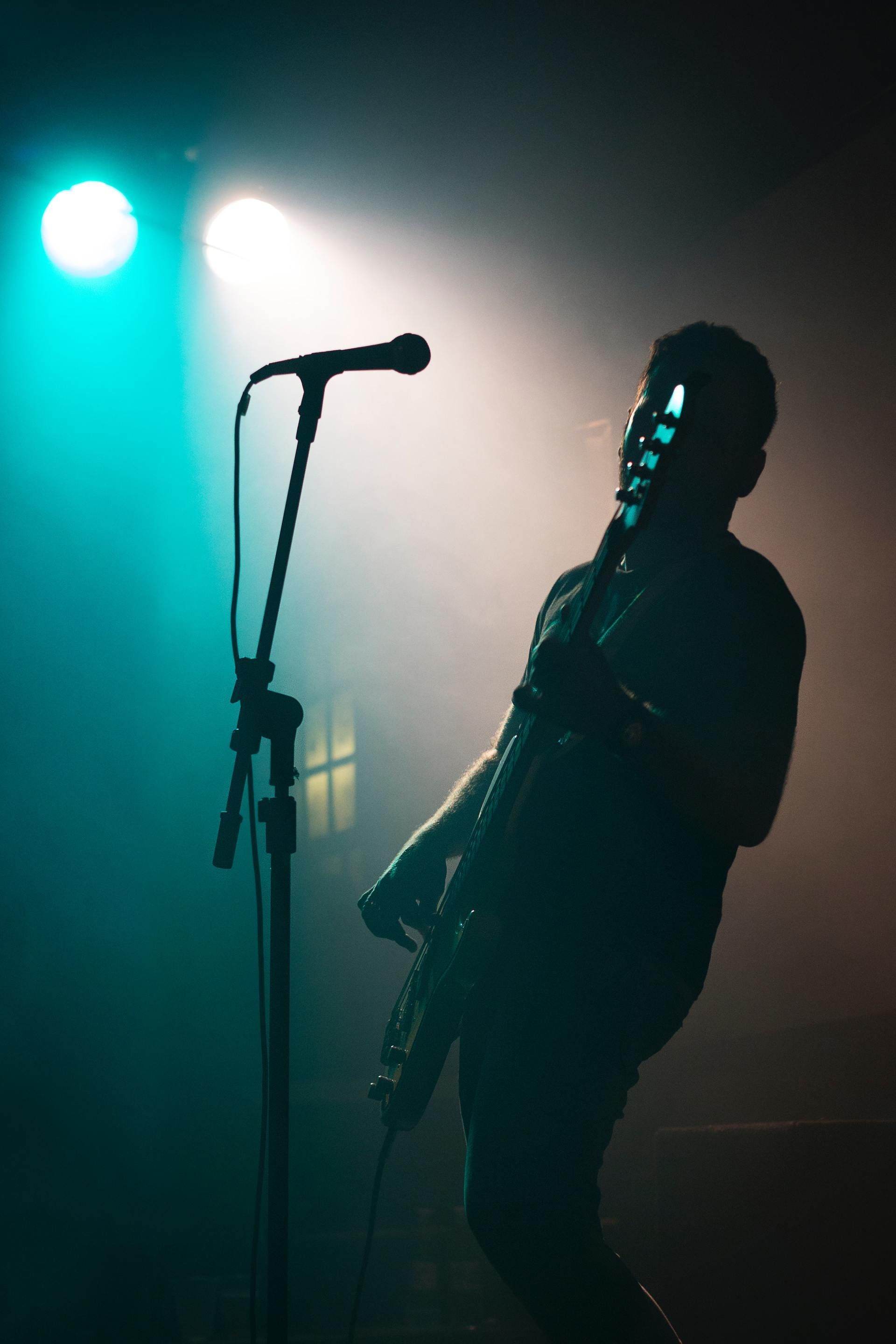 Silhouetted musician playing guitar on a smoky stage under teal and white spotlights