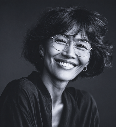 Smiling woman with glasses, short dark hair, in front of a dark backdrop.