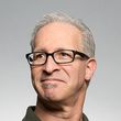 A man wearing glasses and a green shirt is smiling and looking up.