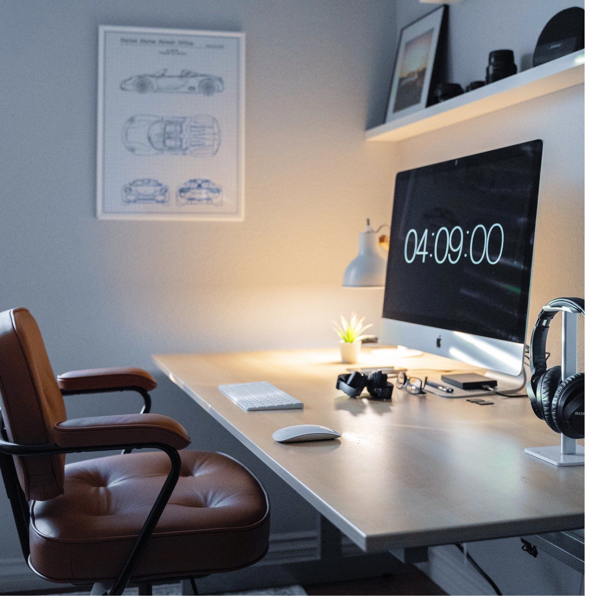 Minimalist home office with desk, computer monitor, brown chair, and soft lamp light