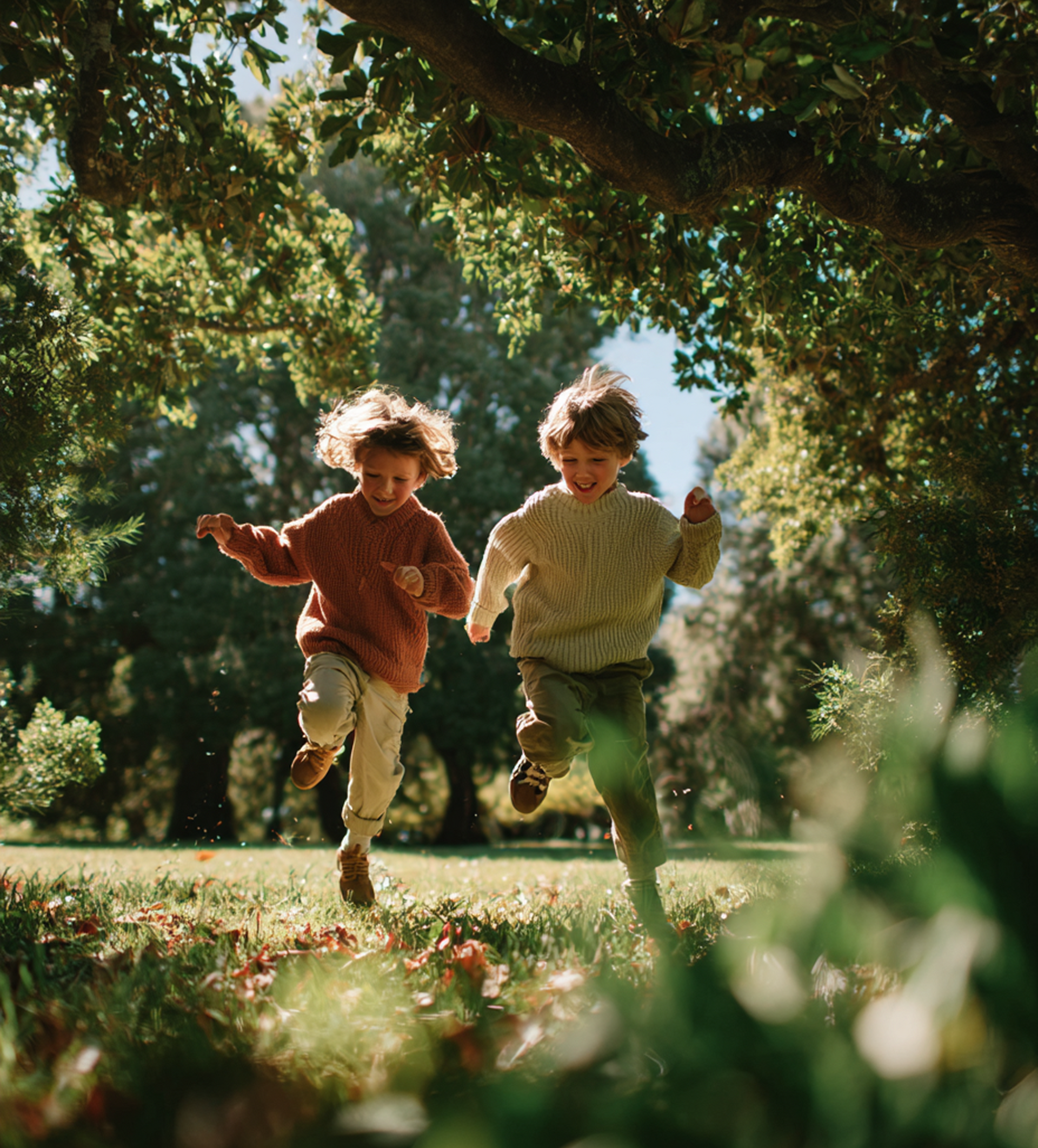 Two children run joyfully through a sunlit park, under trees.