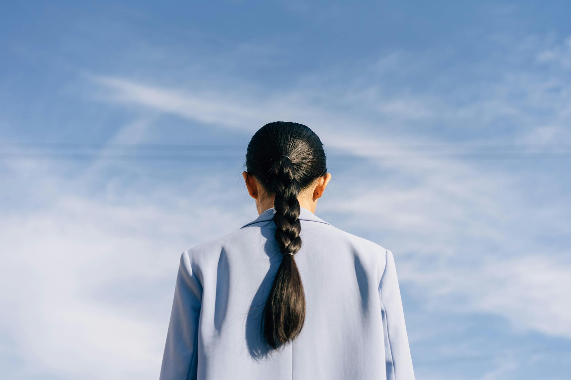Person seen from behind in a light blue jacket, standing against a bright blue sky
