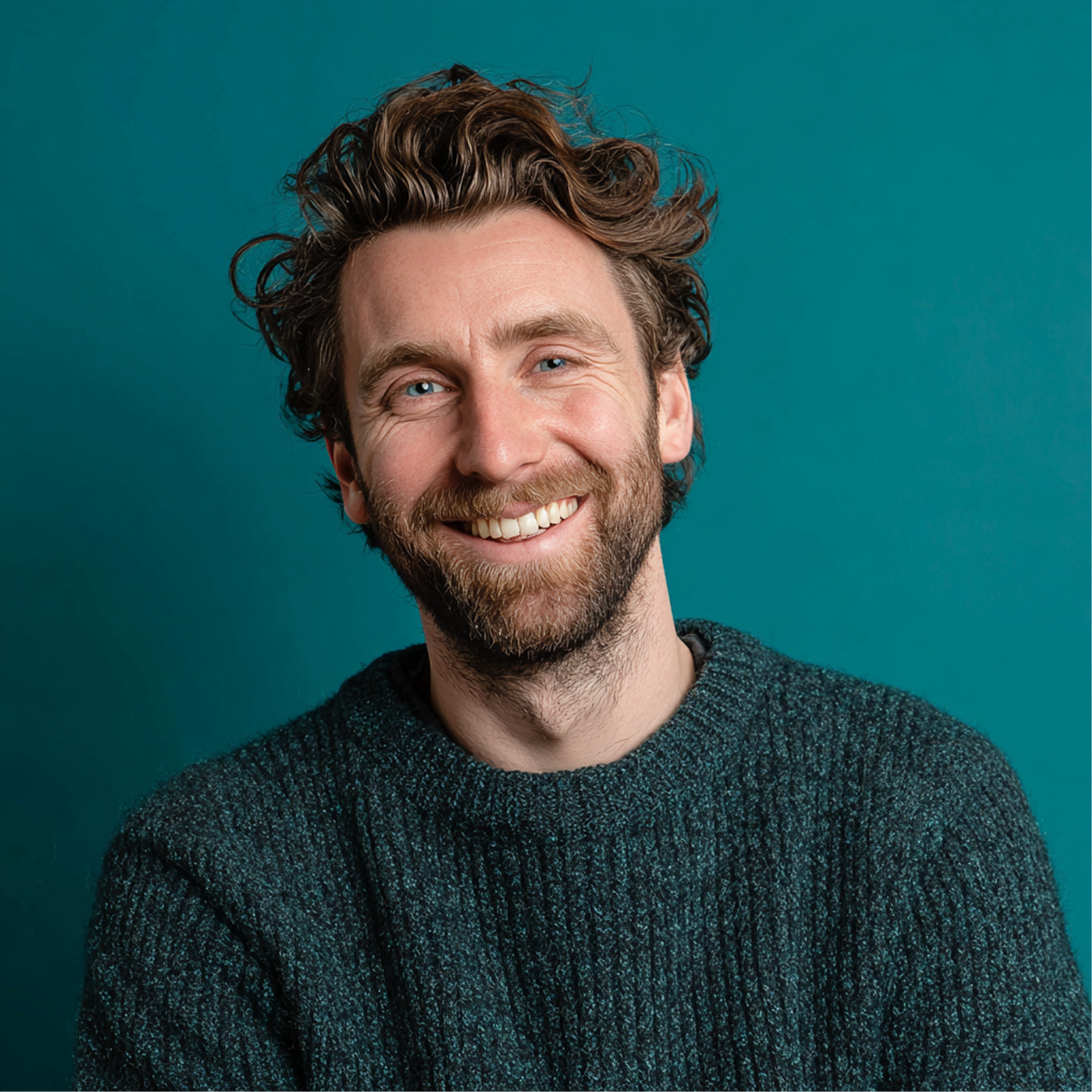 Man with curly brown hair, beard, and a warm smile wearing a blue-green sweater against a teal background.