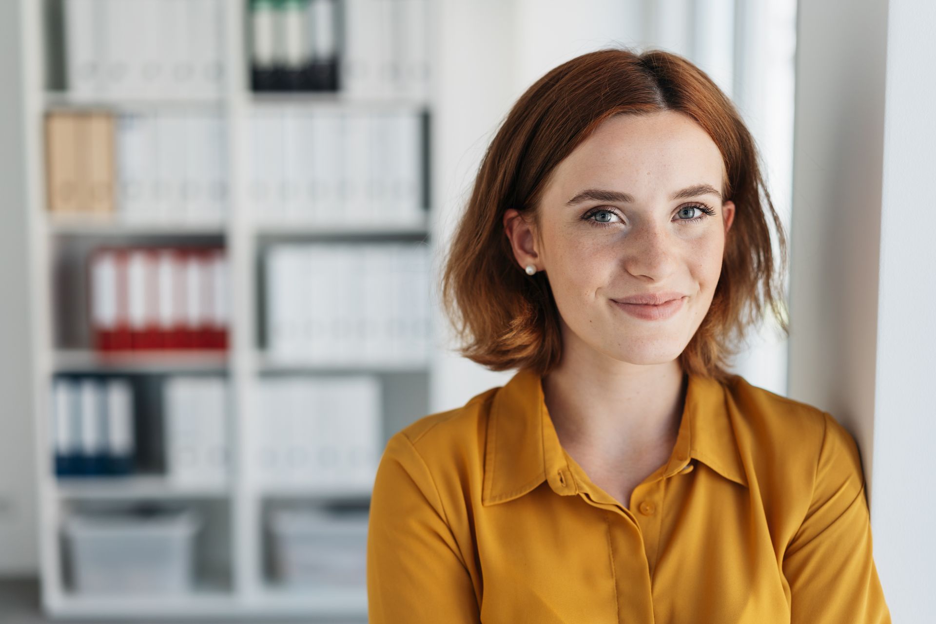 A woman in a yellow shirt is leaning against a wall and smiling.