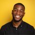 Smiling man in a black shirt against a bright yellow background