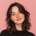 Portrait of a smiling woman with wavy brown hair against a pink background