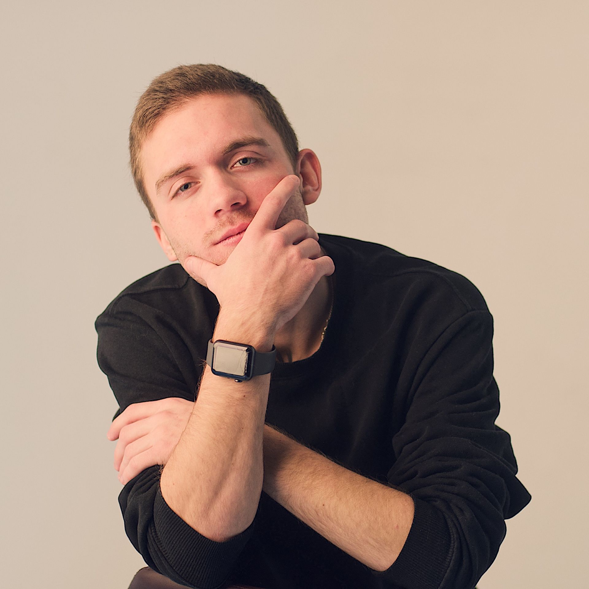 Eine Person in einem schwarzen Pullover posiert nachdenklich mit verschränkten Armen und der Hand am Kinn