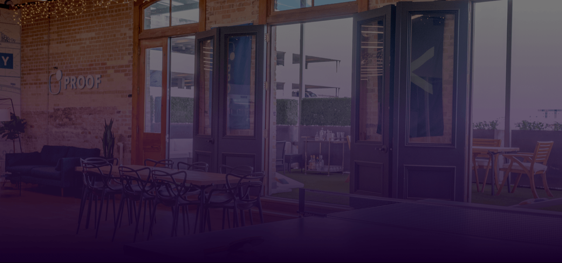 Outdoor cafe with empty tables and chairs under a large awning beside glass storefront windows