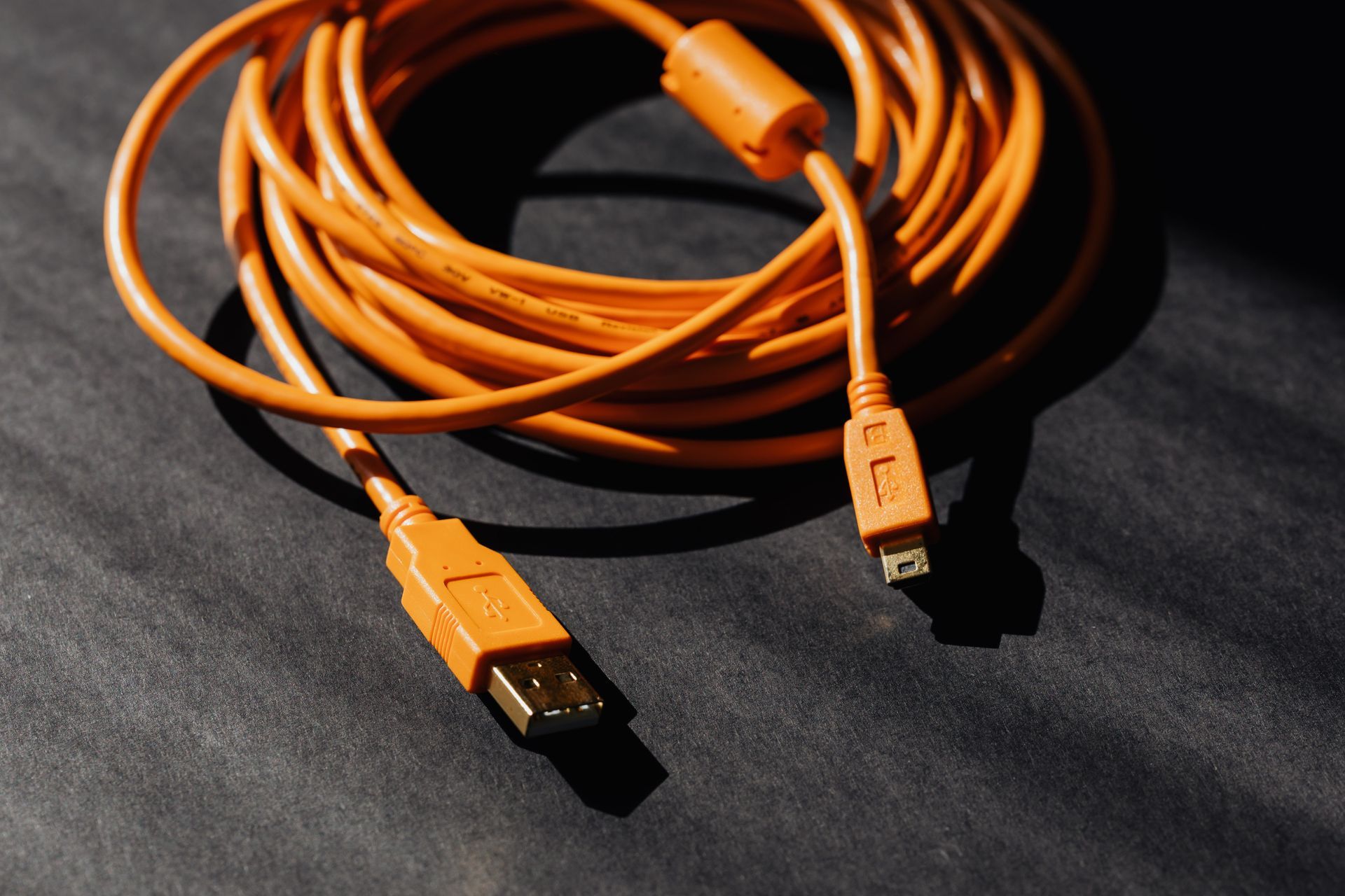 A coiled orange USB cable with a Type-A connector and a smaller rectangular connector, set against a dark background.