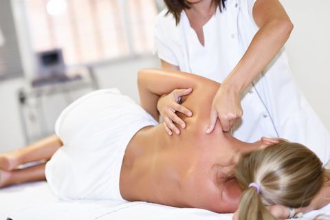 Een massagetherapeut rekt de nek en bovenrug van een cliënt op een behandeltafel.