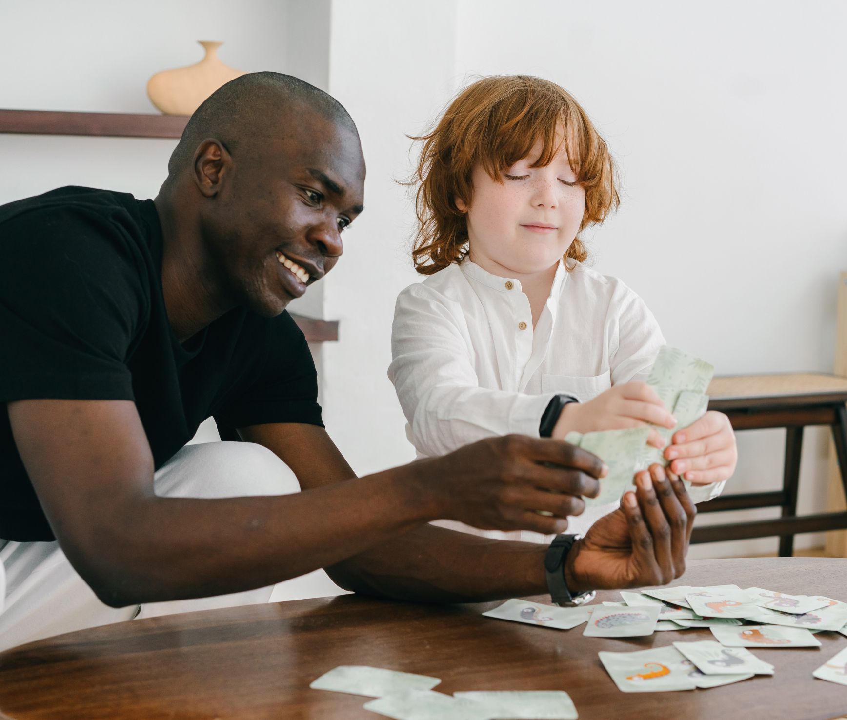 Two people counting cash at a table, with scattered cards and papers in a bright room