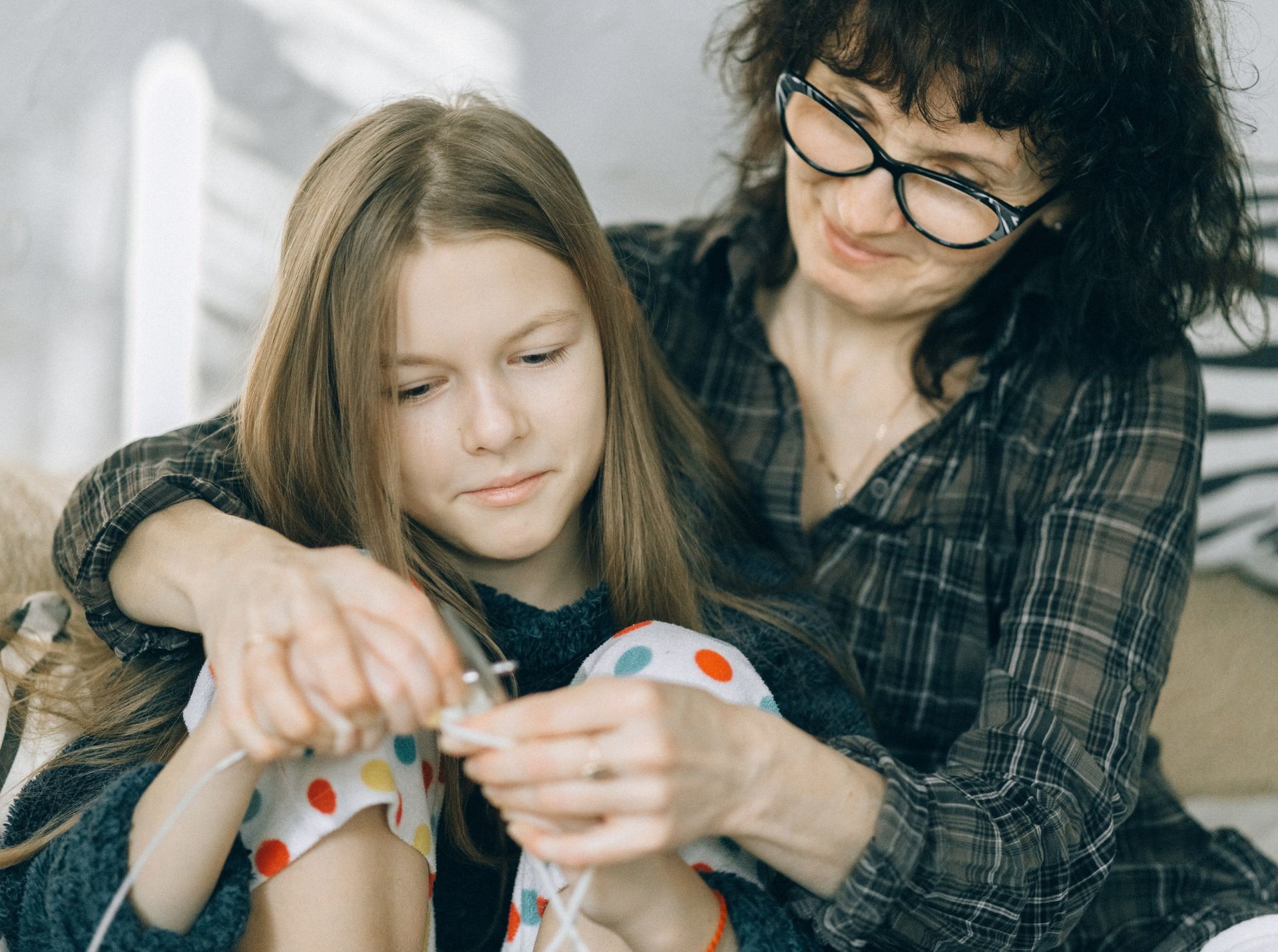 Two people sitting together, with one helping the other hold a small object indoors