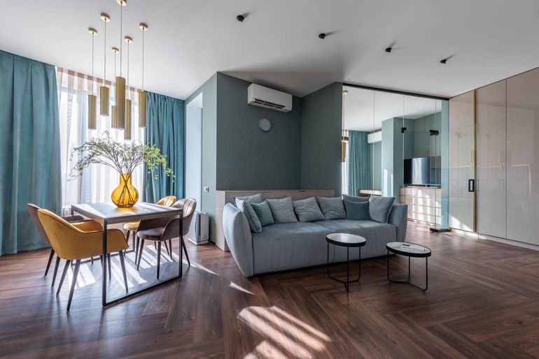 Modern living room with blue walls, wood floors, sofa, dining table, and curtains.