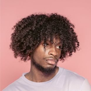 A man with curly hair and a beard is wearing a white shirt.