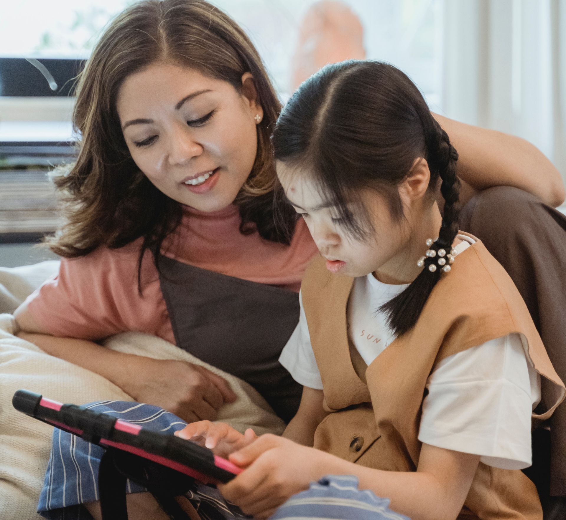 Een vrouw en een kind kijken samen naar een tablet binnenshuis. De vrouw heeft een arm om het kind heen geslagen.