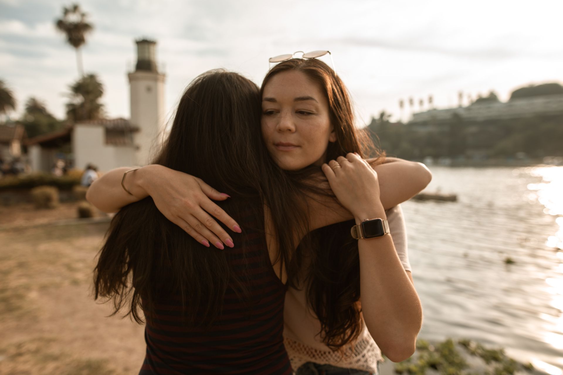 Two women are hugging each other on the beach near the water.