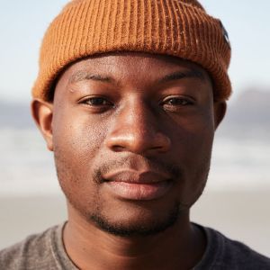 Man wearing a brown beanie, looking directly at the camera with a neutral expression.
